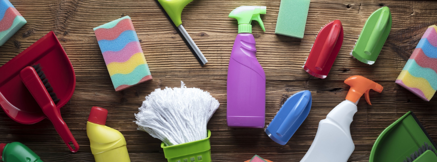 Assorted colorful cleaning supplies and tools arranged on a rustic wooden background